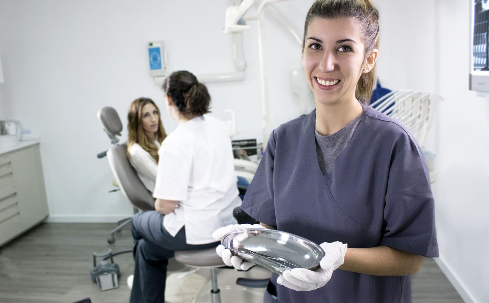 Una auxiliar de CMDent sonríe en el gabinete dental mientras la doctora atiende a una paciente